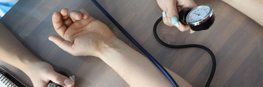 Doctor measuring blood pressure with tonometer at table in clinic closeup. Diagnosis and treatment of arterial hypertension concept