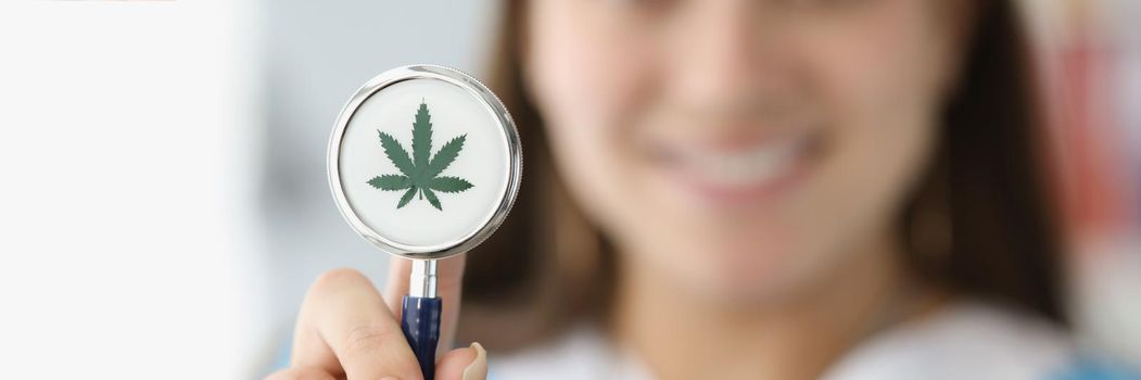 Doctor holding stethoscope with drawn marijuana leaf closeup. Narcotic drug treatment concept