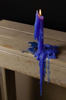 blue candle lit and melted on a wooden table with a black background