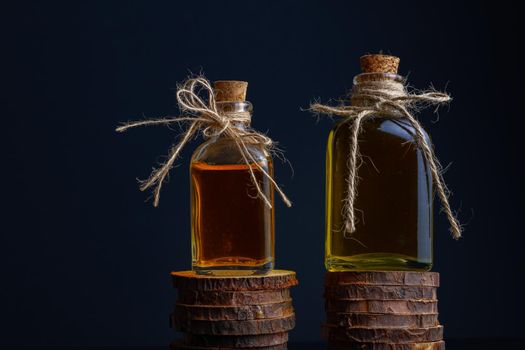 close-up of two glass bottles with cork stopper and raffia string with rosemary oil and rose oil on a dark background
