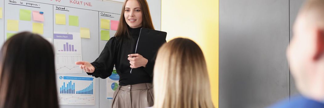 Woman coach explaining information to students in front of blackboard with graphs. Business seminars and meetings concept