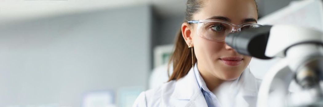 Woman scientist chemist looking through microscope in laboratory. Chemistry lessons at school concept