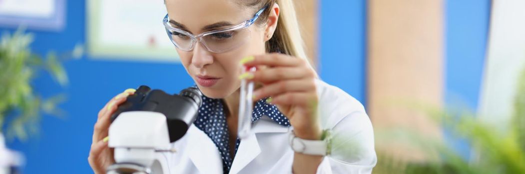 Woman scientist chemist looking through microscope and holding test tube. Laboratory diagnostics of internal diseases concept