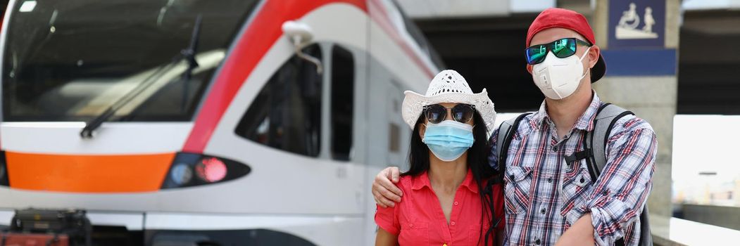 Young couple in protective medical masks standing near train with tickets in their hands. Traveling during covid19 pandemic concept