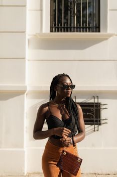 Young black female posing with style while holding her purse in the street during a summer sunset