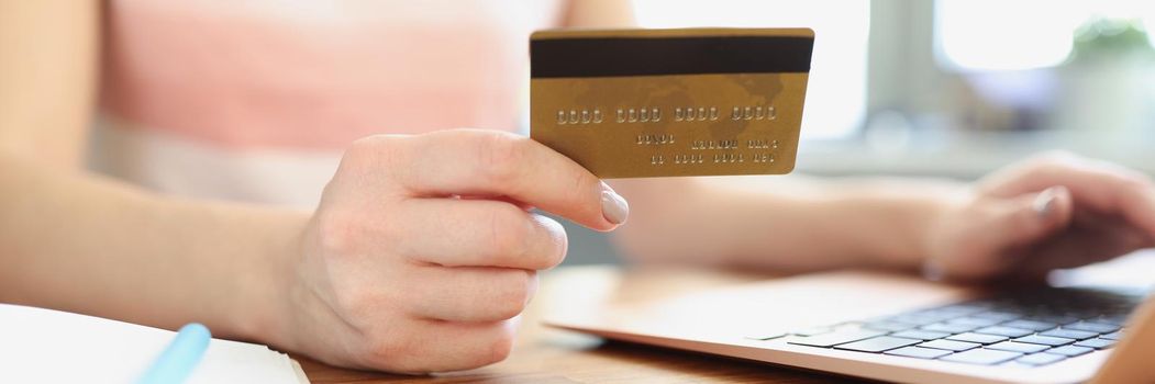 Female hands holding credit bank card in front of laptop closeup. Online shopping concept