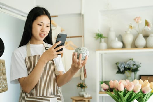 Happy asian female, small stock business owner holding phone product photography checking commercial shipping delivery order on smartphone using mobile app technology.