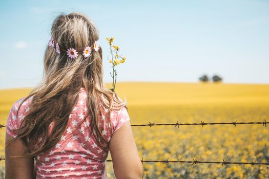 Hippie woman standing by fields of flowering canola in Spring.