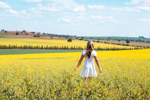 Woman wanders in fields of flowers.  She is wearing a simple white cotton dress