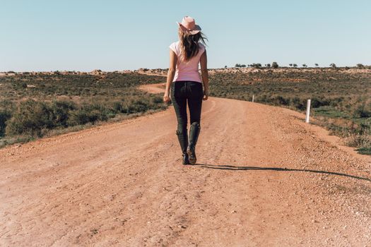 A woman wearing jeans and t-shirt walking dusty roads of outback Australia