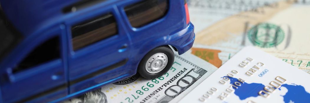 Blue toy car standing on dollar bills and plastic credit card closeup. Buying car concept