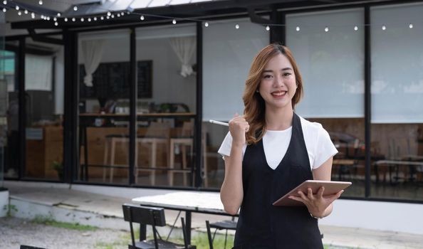 Attractive beautiful young Asian female restaurant or coffee shop waitress noting a customer's order on a digital tablet..