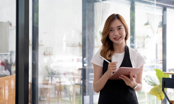 Portrait, Beautiful millennial Asian female waitress or restaurant owner standing in front of her restaurant entrance. Restaurant or coffee shop business owner concept..