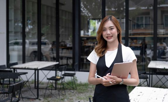 Portrait, Beautiful millennial Asian female waitress or restaurant owner standing in front of her restaurant entrance. Restaurant or coffee shop business owner concept..