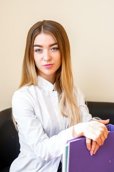 Portrait of beautiful young caucasian businesswoman with folders standing and looking at the camera in the office