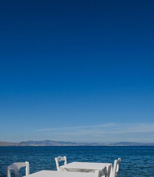 White restaurant tables on the beach in summer - travel, vacation and summer concept. The perfect lunch with a sea view