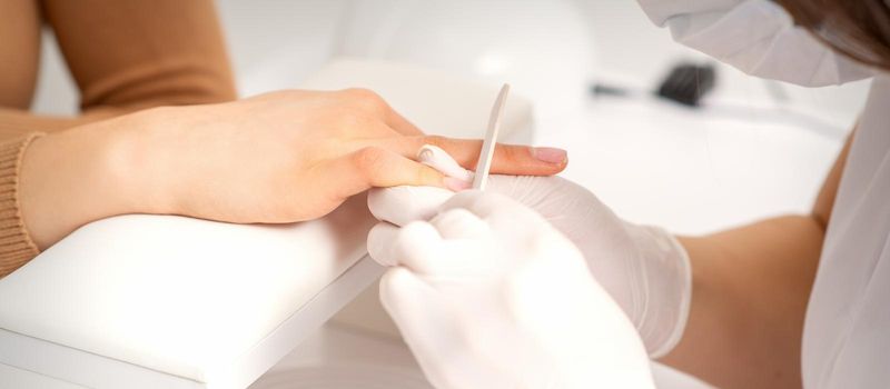 Close up of the hand of young woman receiving the nail file procedure in a beauty salon