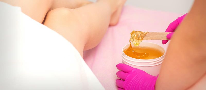Cosmetologists waxing female legs with hot sugar paste in a beauty spa salon