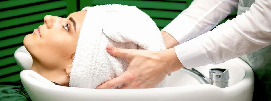 Side view of female hairdresser dries the female client's hair with a towel in the sink at a hair salon