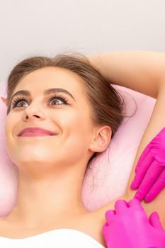 Closeup of a beautiful young caucasian smiling woman receiving waxing her armpit by hands of a beautician in a medical spa