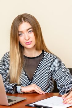 Portrait of a beautiful young caucasian woman sitting at the table working with documents looking at the camera in an office