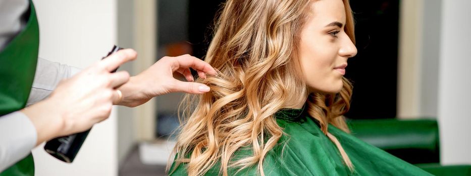 Side view of female hairdresser using hairspray fixing client's female hair in a hair salon