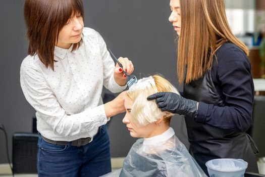 Two female hairdressers dyeing hair of young caucasian woman in hair salon