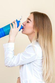 Side view of beautiful young caucasian woman is drinking water from plastic bottle against a beige background