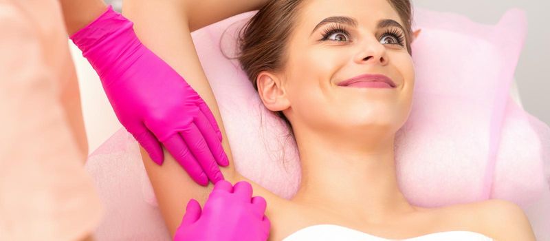 Beautiful young caucasian smiling woman receiving waxing her armpit by hands of a beautician in a medical spa
