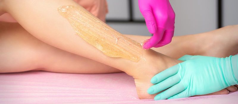 Two female cosmetologists waxing woman's legs with hot sugar paste in a beauty spa salon