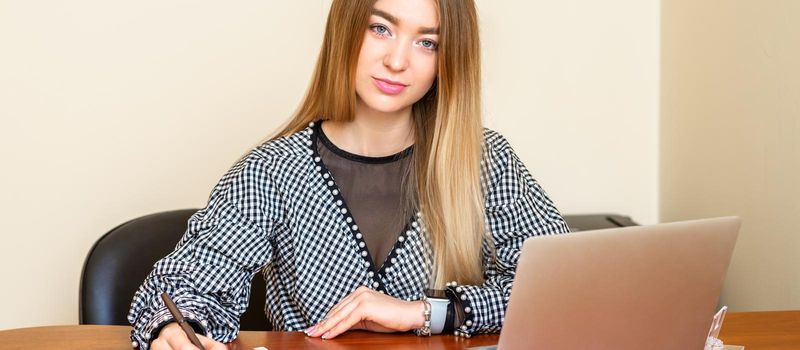 Portrait of a beautiful young caucasian woman sitting at the table working with documents looking at the camera in an office