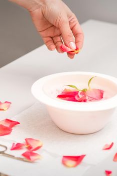 Beautician's female hands preparing manicure bath with red and pink roses petals on the table in spa