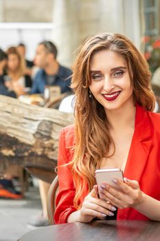 Beautiful young travel woman with smartphone sitting at the table looking at camera in cafe outdoors