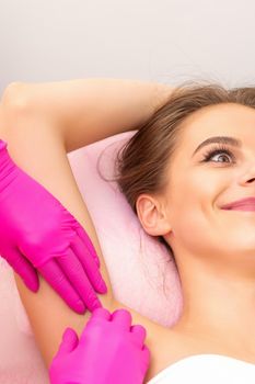 Closeup of a beautiful young caucasian smiling woman receiving waxing her armpit by hands of a beautician in a medical spa