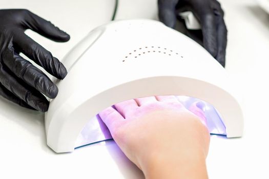 White female hand with manicured nails inside of UV lamp in a nail salon