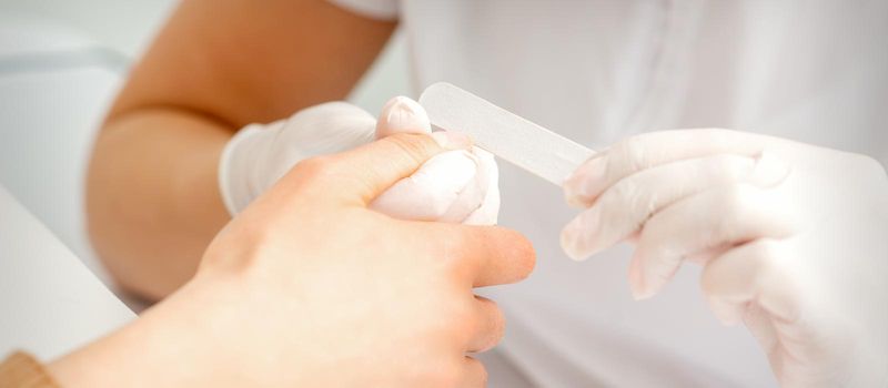 Close up of the hand of young woman receiving the nail file procedure in a beauty salon