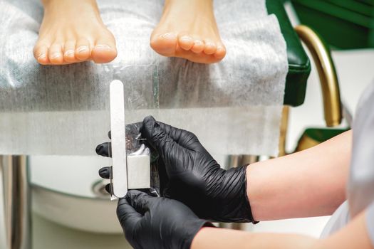 Nail file tool in hands of chiropodist before procedure files nails on toes in a nail salon