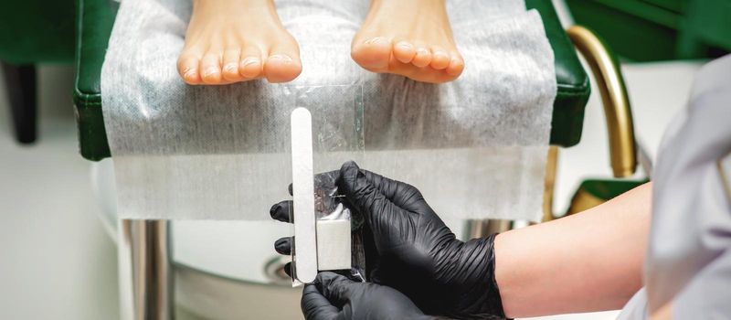 Nail file tool in hands of chiropodist before procedure files nails on toes in a nail salon