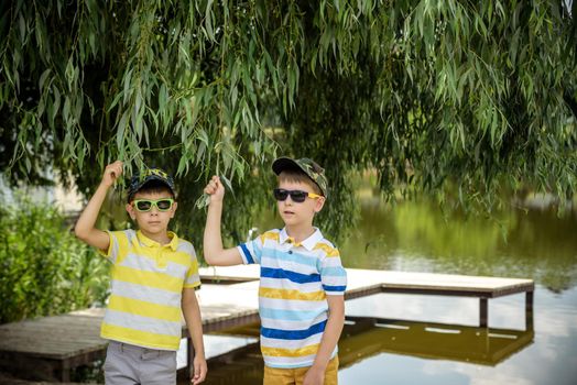 Siblings, brother, hugs. Two children, older boy and his younger brother standing on the shore of the lake near old tree. Summertime holiday concept leisure time on nature.