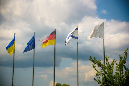 The flag of the European Union and flags of Ukraine, Israel, Germany flutter in the wind in different directions against the blue sky. Bottom side view.