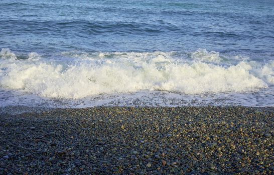 Sea shore with pebbles, wet sea pebbles on the beach and quiet sea surf. Restless sea and waves.