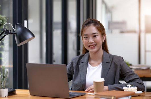 Charming Asian woman working at the office using a laptop Looking at the camera..