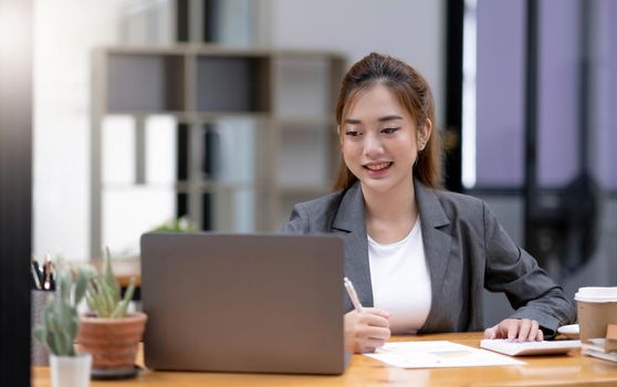 Beautiful young asian woman sitting at coffee shop using laptop. Happy young businesswoman sitting at table in cafe with tab top computer..