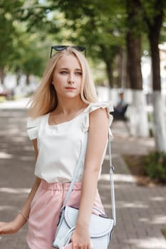 A stylish young girl walks around the city with coffee and wearing sunglasses. The concept of an urban lifestyle.