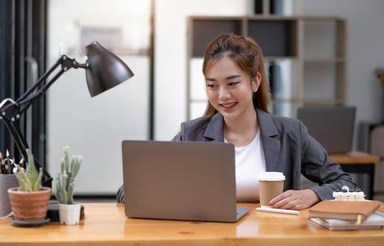 Beautiful young asian woman sitting at coffee shop using laptop. Happy young businesswoman sitting at table in cafe with tab top computer..