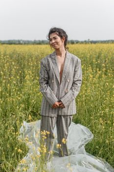 An Asian model poses in a field of yellow flowers for a clothing brand, polyethylene is the main props for a photo shoot. The concept of manufacturing clothing from recycled plastic. A woman in a pantsuit is standing on a plastic bag.