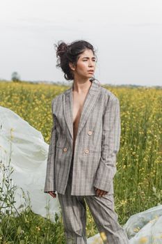 An Asian model poses in a field of yellow flowers for a clothing brand, polyethylene is the main props for a photo shoot. The concept of manufacturing clothing from recycled plastic. A woman in a pantsuit is standing on a plastic bag.