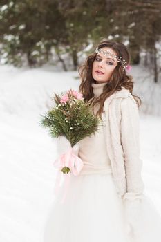 Beautiful bride in a white dress with a bouquet in a snow-covered winter forest. Portrait of the bride in nature.