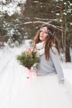 Beautiful bride in a white dress with a bouquet in a snow-covered winter forest. Portrait of the bride in nature.