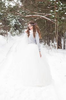 Beautiful bride in a white dress with a bouquet in a snow-covered winter forest. Portrait of the bride in nature.